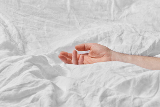Close up of male hand lying on white crumpled bed sheet