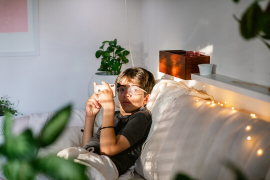 Pretty thirteen boy lying on sofa using phone