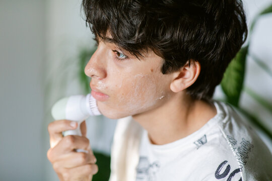 Teenager cleaning face with electric cleaner at home