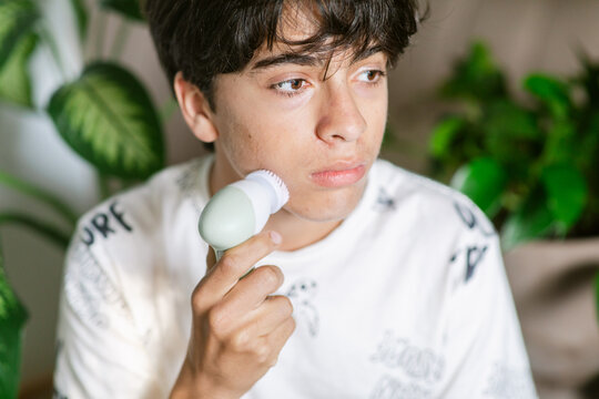 Teenager cleaning face with electric cleaner