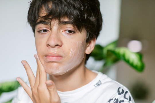 Teenager moisturizing his face portrait