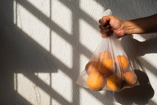 Oranges in a white recyclable mesh bag held by a male right hand
