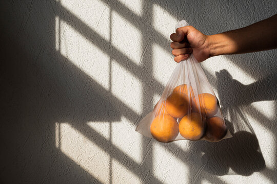 Oranges in a white recyclable mesh bag held by a male right hand
