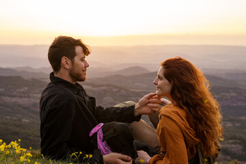 Portrait of young loving couple in the mountain at sunset with dog