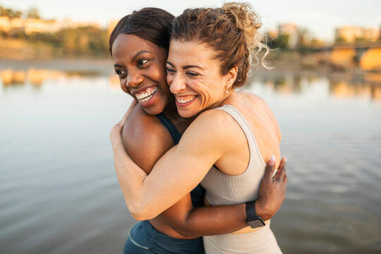 Middle-aged multiracial female friends embrace on a river jetty