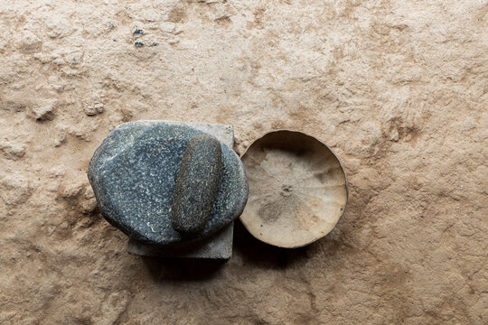 a stone metate on the ground next to a pumpkin gourd