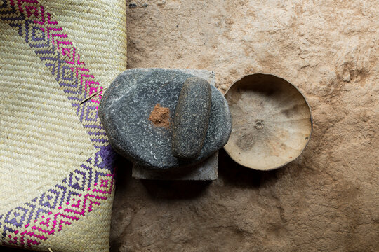 a stone metate on the ground next to a pumpkin gourd and petate