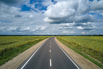 Aerial view of intercity road between green agricultural fields with fast driving cars. Top view from drone of highway traffic