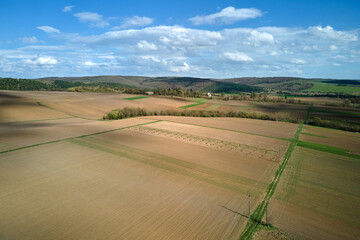 Fototapeta na wymiar Aerial view of plowed agricultural fields with cultivated fertile soil prepared for planting crops between green woods in spring