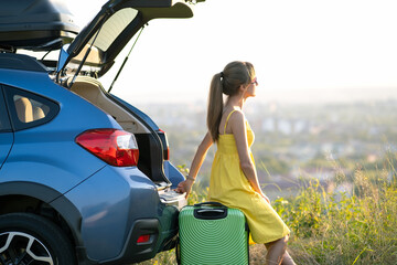 Fototapeta na wymiar Young woman resting on a green suitcase near her car in summer nature. Travel and vacations concept.