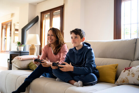 Cheerful boy with mother playing videogame on sofa