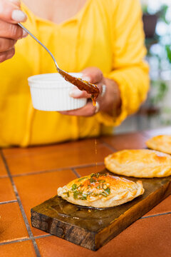 A woman in a yellow shirt putting sauce on an Argentinian empanada 
