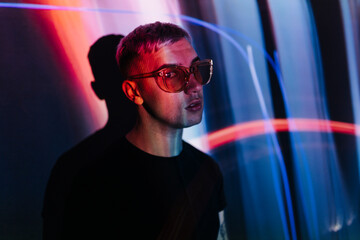 Stylish man in sunglasses in dark room with neon lights
