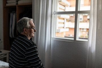 Elderly man looking out the window of his room