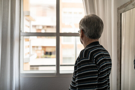 Elderly man looking out the window of his room