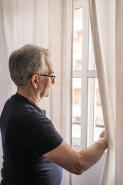 Elderly man looking out the window of his room
