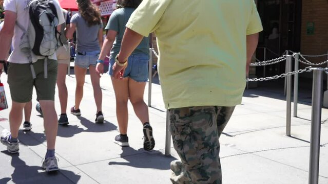 This POV video shows the rear side of an obese man walking through a crowd.