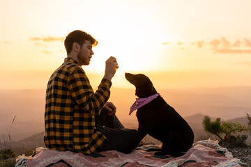 Man and dog sitting on nature at sunset looking at the landscape