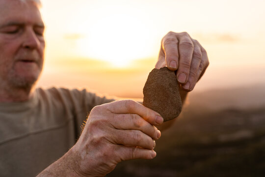 closeup of  senior man hands in nature holding stone against sky