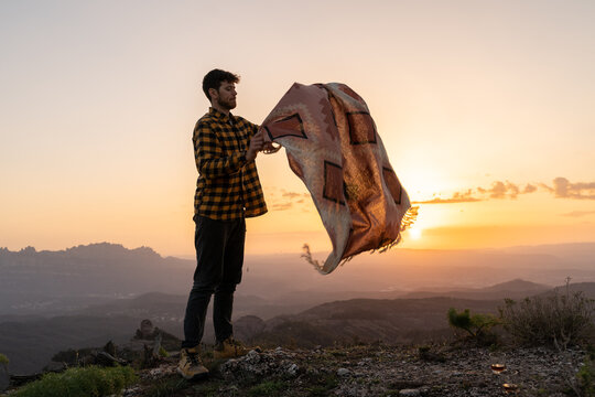 Man shaking picnic blanket in nature at sunset
