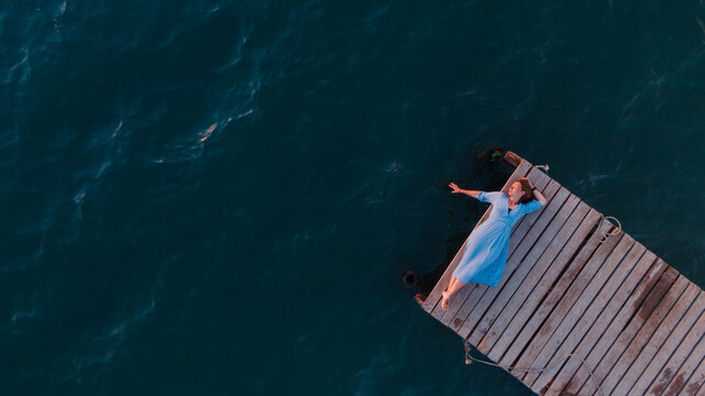 young woman laying on the pier at the sunset, drone overhead