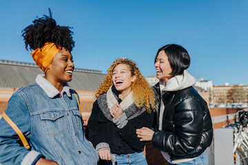 Cheerful multiethnic friends hugging on rooftop