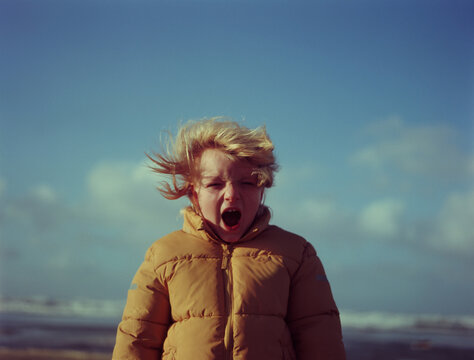 A kid shouting on a beach in a windy day