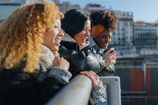 Cheerful multiethnic friends looking at city from balcony