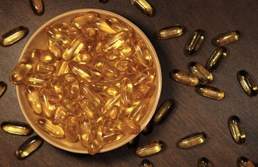 cup of omega 3 capsules and some spilled around it.
omega 3 fish oil capsules scattered on dark wooden table.