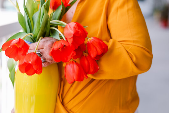 Crop woman holding yellow vase with red tulips 