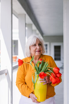 Senior woman holding yellow vase with red tulips 
