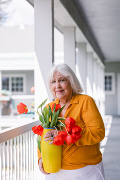 Senior woman holding yellow vase with red tulips 