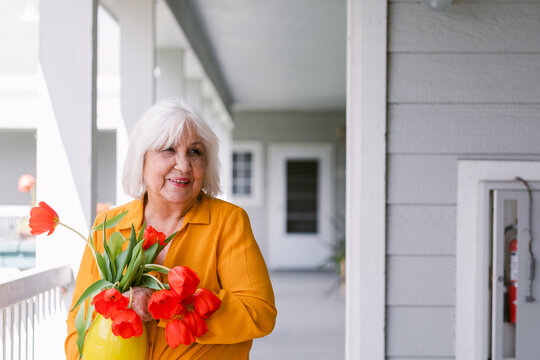 Senior woman holding yellow vase with red tulips 