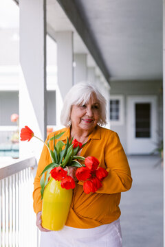 Senior woman holding yellow vase with red tulips 