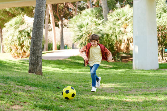 Little boy running after a soccer ball in a park