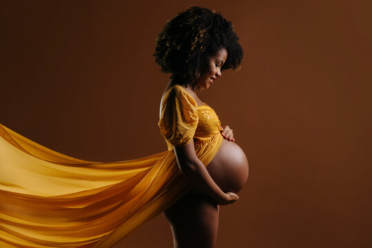 Naked pregnant woman in yellow dress touching belly