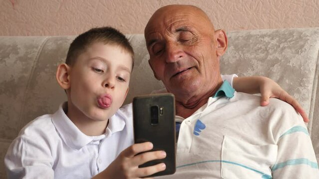 positive caucasian grandchildren 8 years old with grandfather 70 years old hugging pose sitting in front of the phone taking a selfie while being at home.lifestyle grandson and grandfather