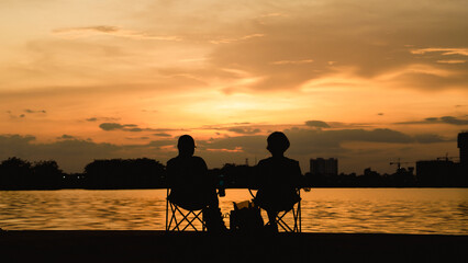 Obraz na płótnie Canvas Happy Asian seniors couple enjoying Silhouette beautiful sunset view at the Thatlunag lake in Vientiane city, Laos. Retirement vacation concept.