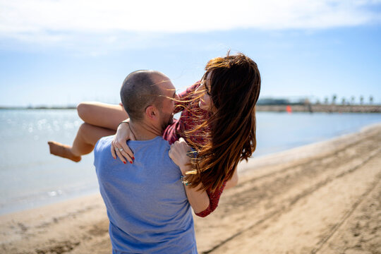 Loving happy guy carrying girlfriend on sandy beach
