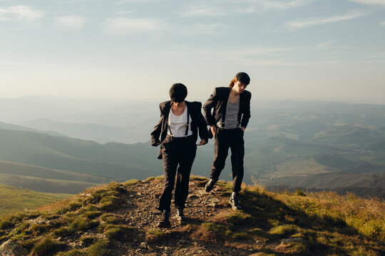 A couple in stylish black suits walks among the mountain landscapes