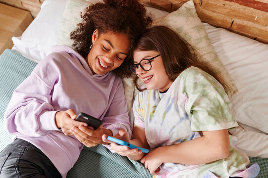 Smiling teen girls using smartphones on a bed