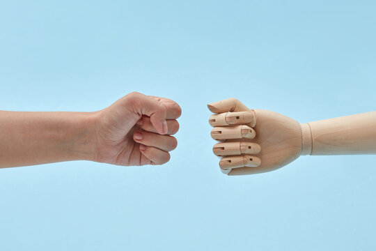 Woman's fist reaching towards a wooden doll's fist.