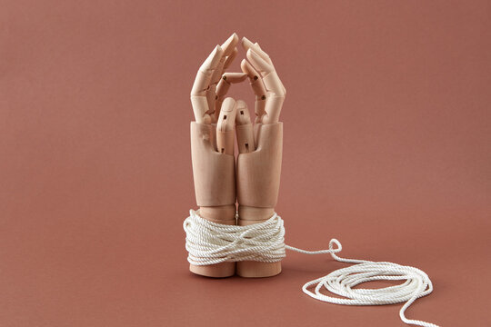 Artificial wooden doll's hands tied with rope.