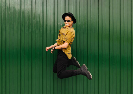 Stylish woman jumping against gren metallic wall