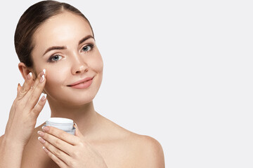 Beauty Woman Face Skin Care. Portrait Of Attractive Young Female Applying Cream And Holding Bottle. Closeup Of Smiling Girl With Natural Makeup And Fresh Skin. Cosmetics