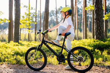 Cute handsome caucasian boy in helmet enjoying riding bike. Child in summer forest learn to balance in bicycle. Summer vacation for inquisitive kid in forest.