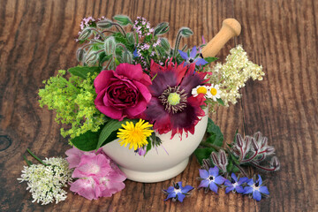 Herbal flower medicine with edible flowers and herbs in a mortar on rustic wood. Alternative nature plant based remedies. Natural health well being concept. On rustic wood background.