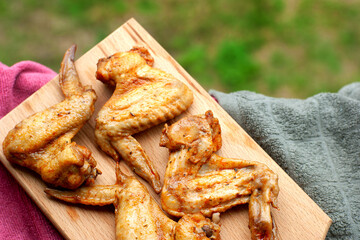 Chicken wings on a picnic. Baked chicken wings on the background of grass on the street. Meat in the form of chicken wings. Food on the windowsill.