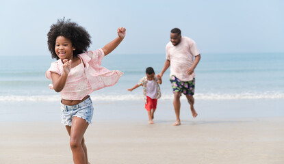 Happy African American kid girl run with family on the beach	