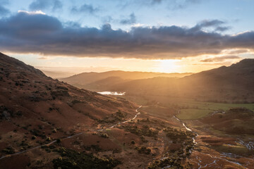 Beautiful aerial drone landscape image of sunrise from Blea Tarn in Lake District during stunning Autumn showing